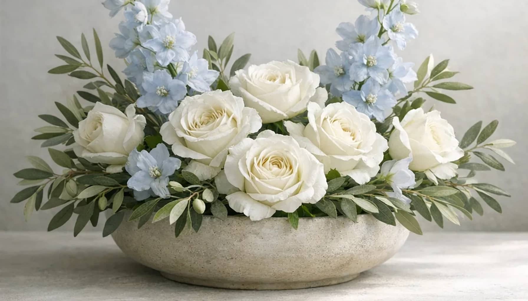 International Day of Non-Violence flower arrangement with white roses, olive branches, pale blue delphinium designed as a respectful peace and solidarity floral guide