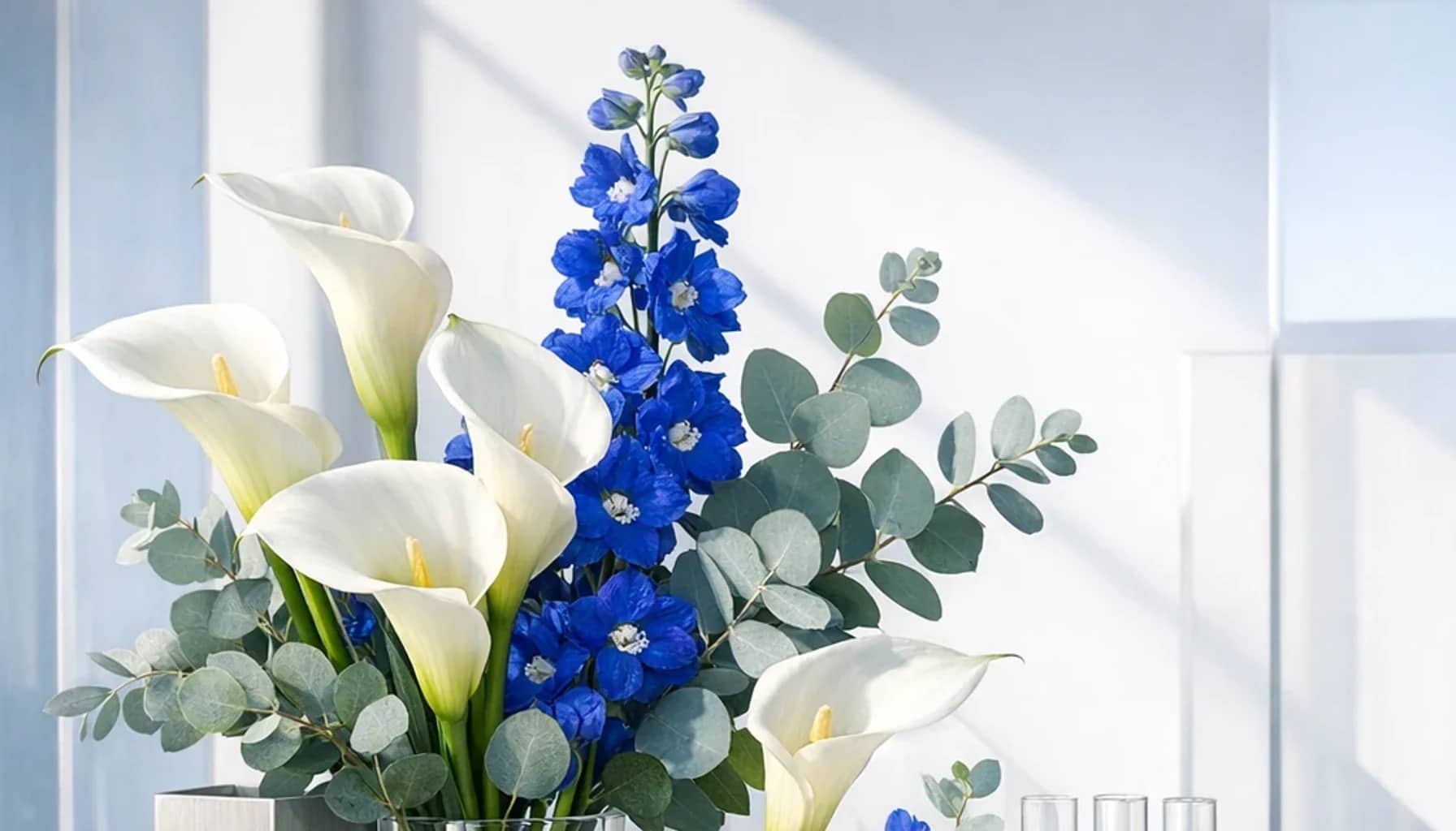 International Day of Women and Girls in Science flower arrangement with white calla lilies, blue delphinium, silver eucalyptus designed as a respectful science and innovation floral guide