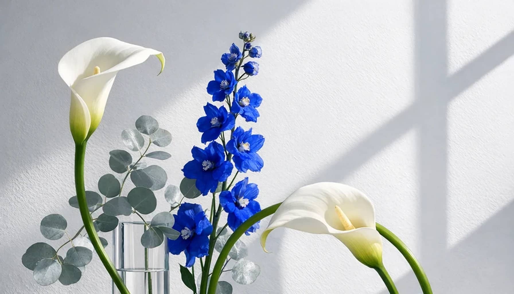World Creativity and Innovation Day flower arrangement with white calla lilies, blue delphinium, silver eucalyptus designed as a respectful science and innovation floral guide