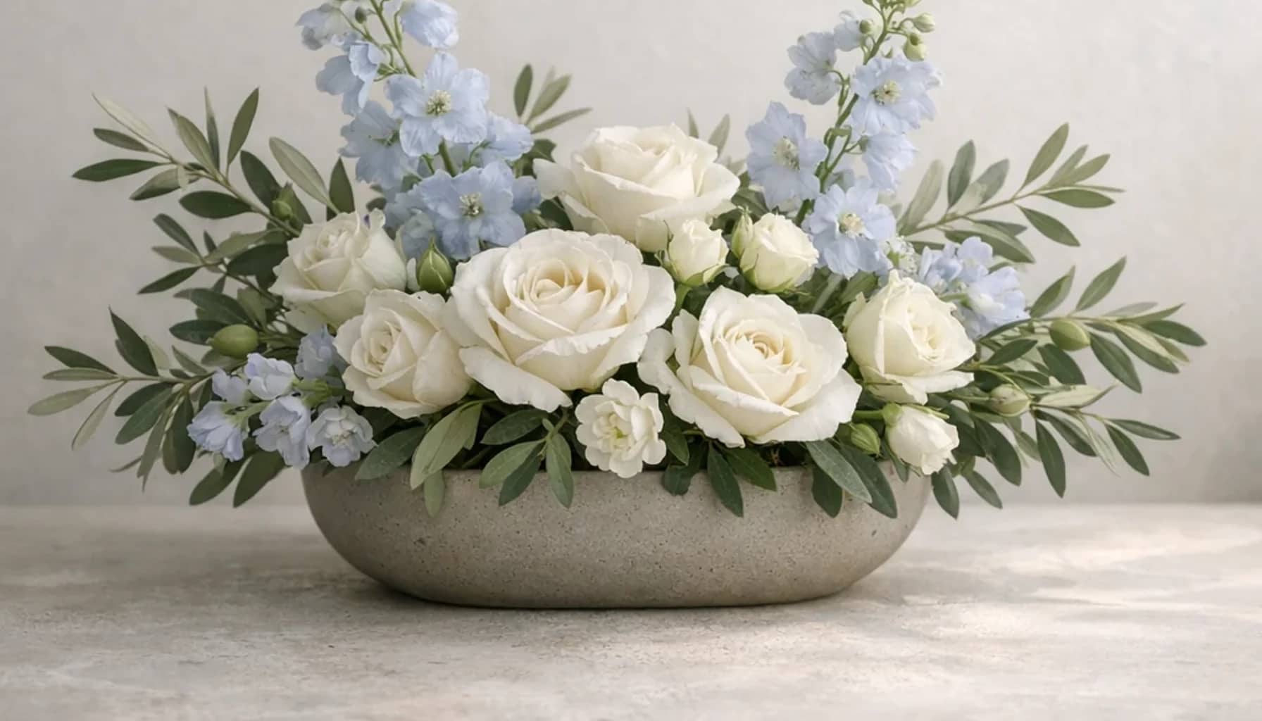 World Refugee Day flower arrangement with white roses, olive branches, pale blue delphinium designed as a respectful peace and solidarity floral guide