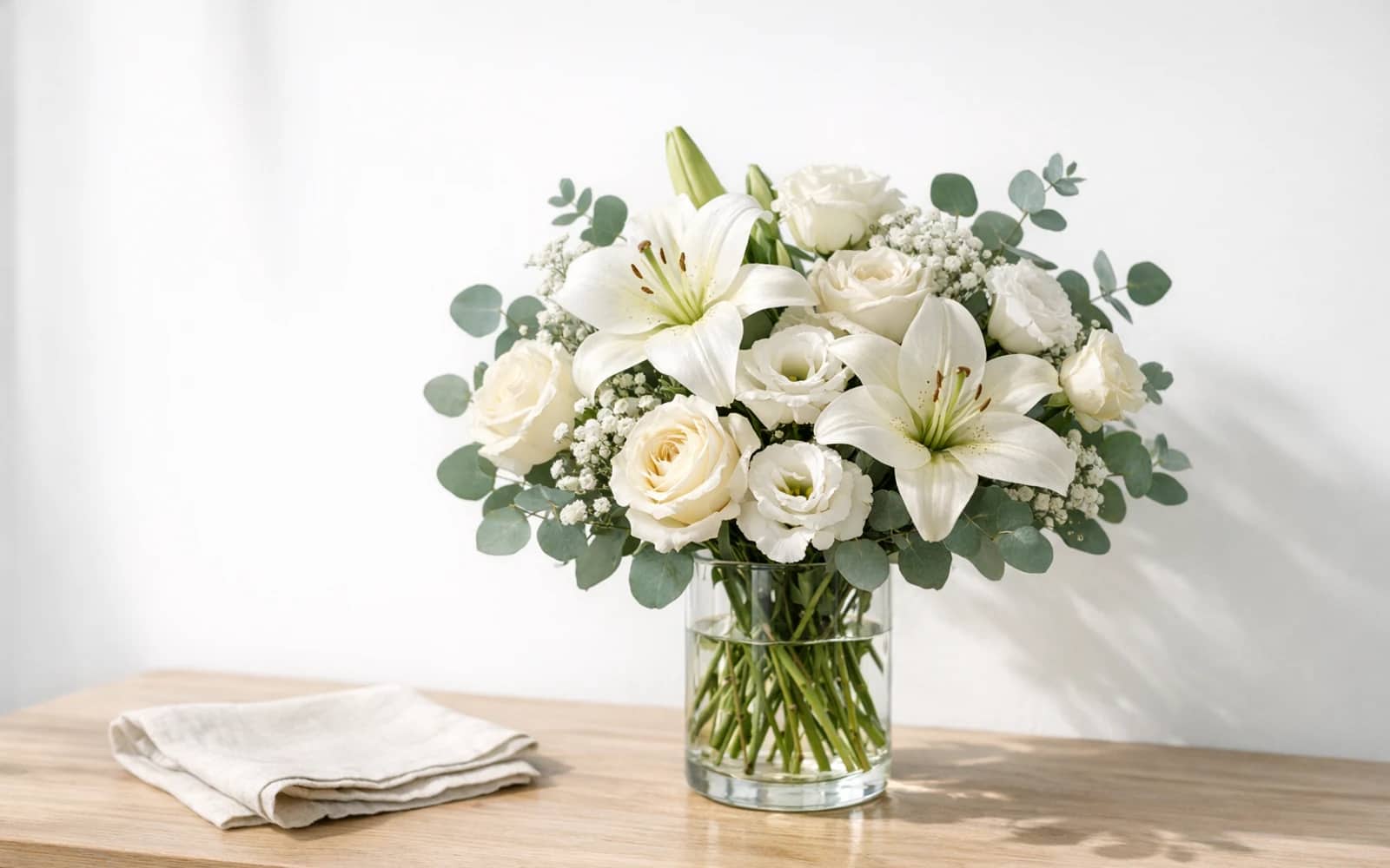 Representative dignified white memorial flower direction with lilies, garden roses, and greenery