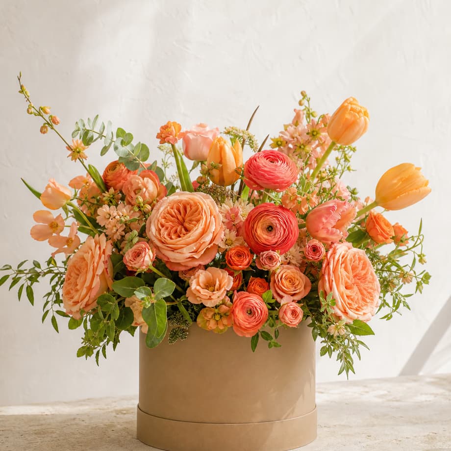 Sunset Garden peach and coral roses, ranunculus, and tulips in a warm taupe flower box