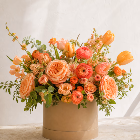 Sunset Garden peach and coral roses, ranunculus, and tulips in a warm taupe flower box